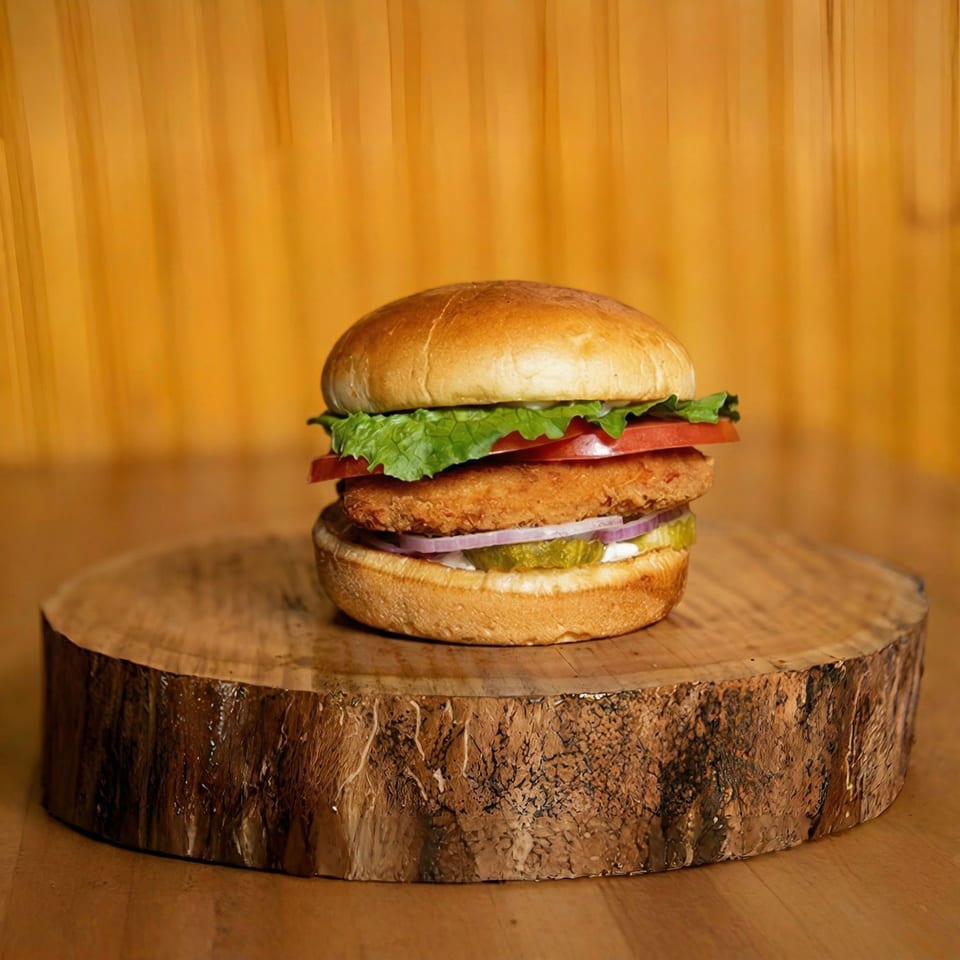 Crispy chicken sandwich with lettuce, tomato, onion, and pickles on a wooden slab.